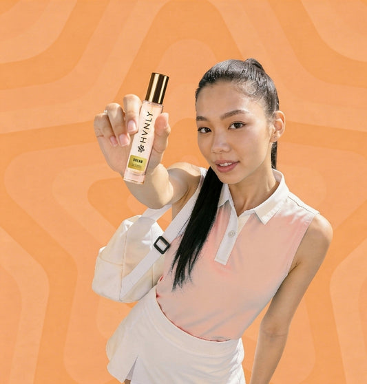 Woman holding a bottle of 'HVNLY Dream' perfume bottle against an orange background