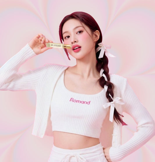 Woman holding a HVNLY's Blossom perfume bottle against a pink background