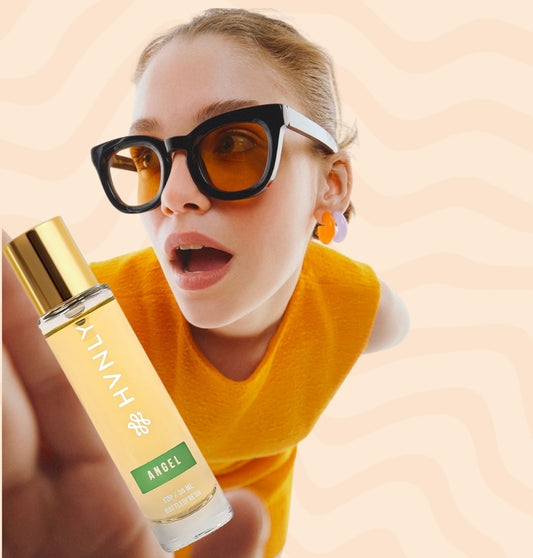 A girl wearing sunglasses and a yellow shirt holding Angel Perfume by HVNLY flexing its size and bottle aesthetic.