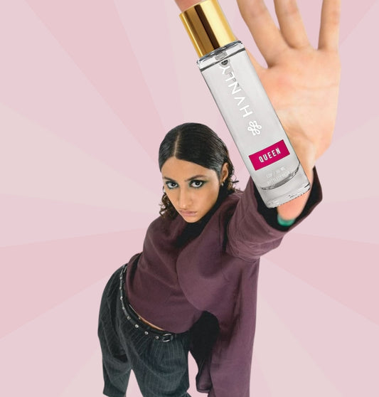 Person holding a bottle of 'Queen' perfume bottle by HVNLY against a pink background