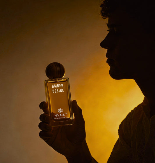 Person holding a HVNLY Amber Desire perfume bottle with a warm glow