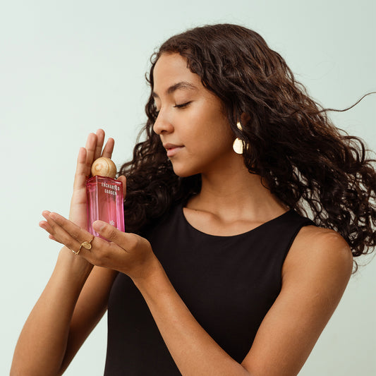 Woman holding a pink perfume bottle showcasing the sleek design and aesthetics of the bottle whilst holding it in her hand.