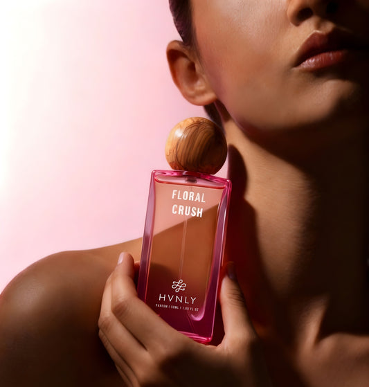 Person holding a pink 'Floral Crush' perfume bottle with wooden cap against a pink background