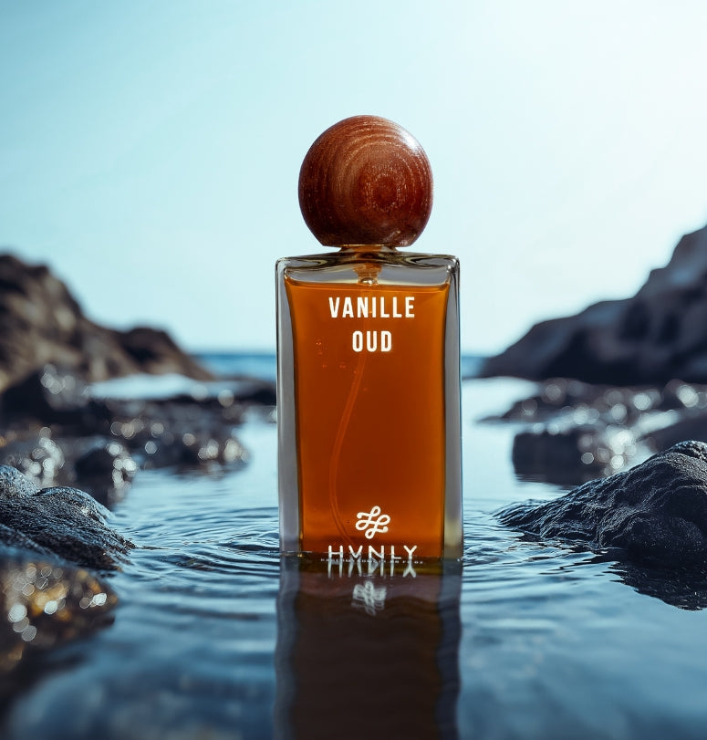 Perfume bottle labeled 'Vanille Oud' by Hvnly on a rock with water in the background