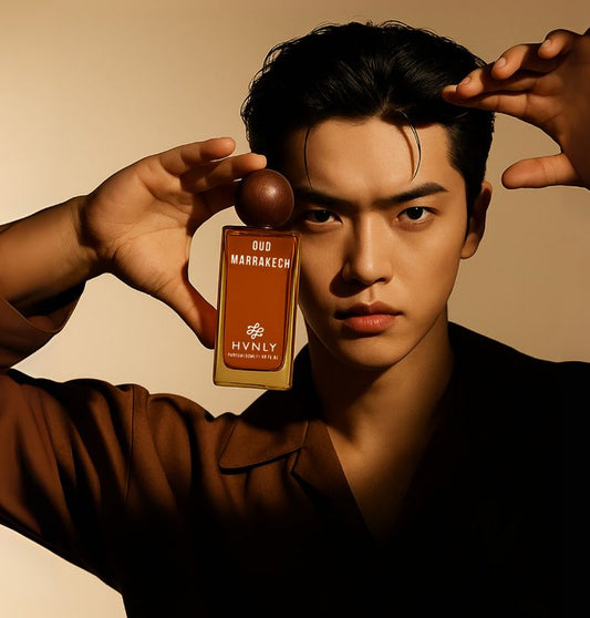 Man holding a perfume bottle of Oud Marrakech by Hvnly against a beige background. Showcasing the sleek design of the bottle and its design aesthetics capturing the original essence of the Oud perfume.
