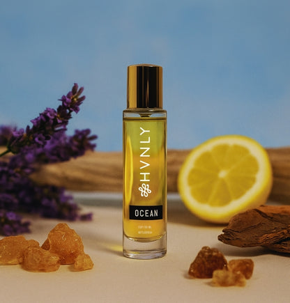 Perfume bottle labeled 'HVNLY Ocean' with lavender, lemon, and frankincense on a blue background showcasing the colorful ingredients of the perfume.