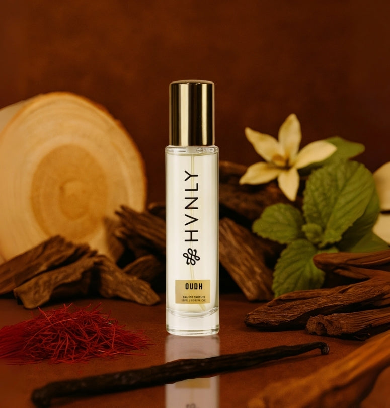 Small bottle labeled 'HVNLY Oudh' with vanilla beans and flowers on a wooden surface showing notes of the perfume
