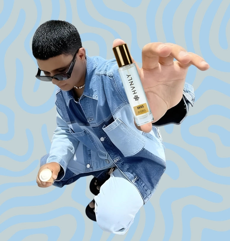 Person holding a bottle of HVNLY's Skies perfume with a blue and gray patterned background showing the compact size of the perfume bottle