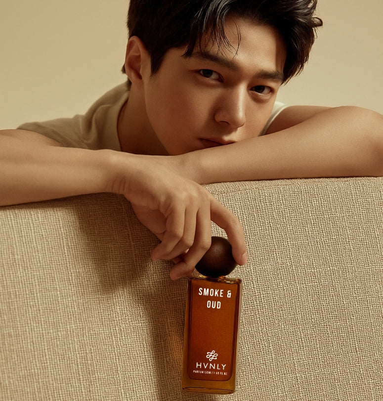 Man holding a bottle of 'Smoke & Oud' perfume by Hvnly on a beige background. It portrays that the perfume serves for chocolate boys as well as for those bad boys out there.