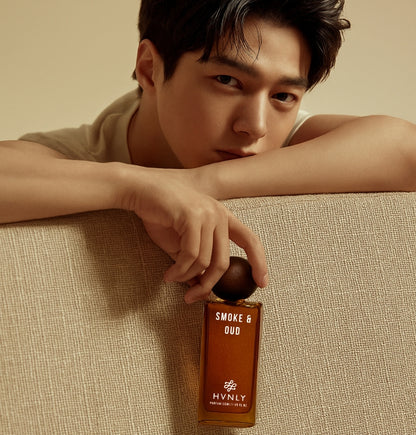 Man holding a bottle of 'Smoke & Oud' perfume by Hvnly on a beige background. It portrays that the perfume serves for chocolate boys as well as for those bad boys out there.