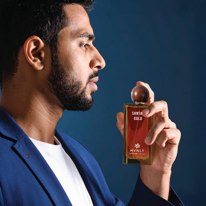 Man holding a Hvnly Santal Gold perfume bottle against a dark blue background