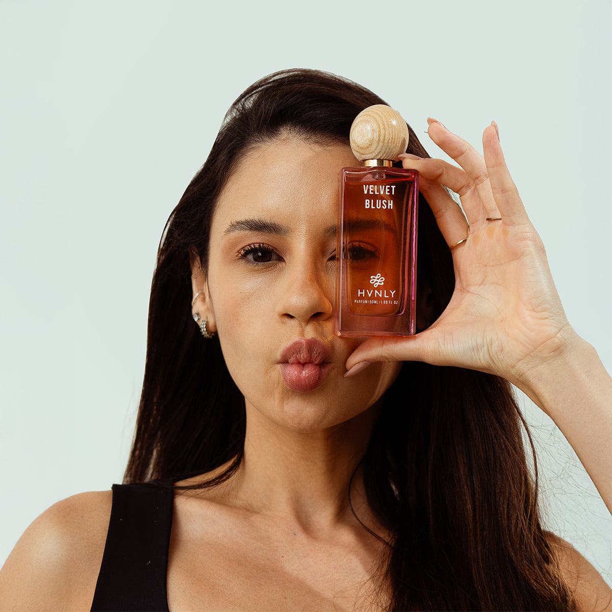 Woman holding a bottle of HVNLY Velvet Blush against a light background showcasing the beauty and aesthetics of the perfume bottle.