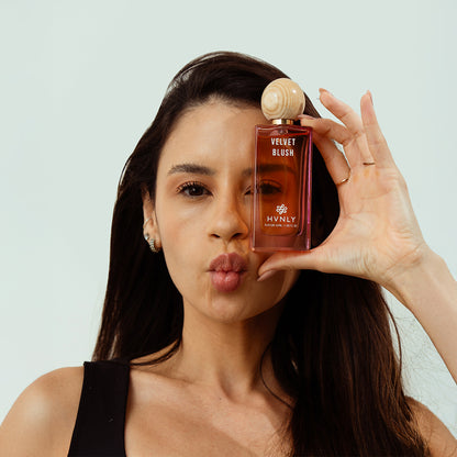 Woman holding a bottle of HVNLY Velvet Blush against a light background showcasing the beauty and aesthetics of the perfume bottle.